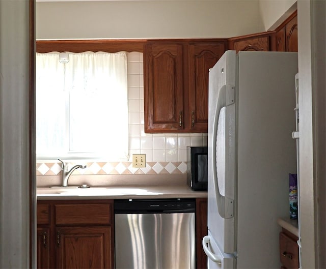kitchen with black microwave, light countertops, freestanding refrigerator, decorative backsplash, and stainless steel dishwasher