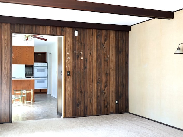 carpeted empty room with baseboards, beamed ceiling, a ceiling fan, and wood walls