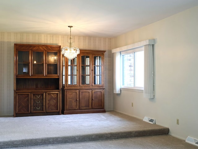 unfurnished dining area with an inviting chandelier, baseboards, carpet flooring, and visible vents