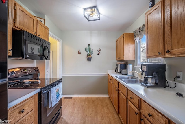 kitchen featuring brown cabinetry, light countertops, a sink, light wood finished floors, and black appliances