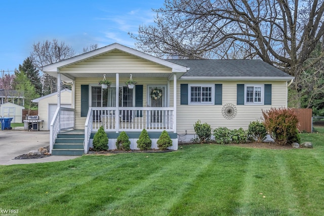 single story home with a shingled roof, covered porch, an outdoor structure, and a front lawn