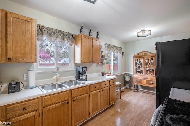 kitchen with a sink, light countertops, black appliances, and light wood-style flooring