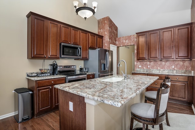kitchen with a sink, dark wood-style flooring, appliances with stainless steel finishes, and light stone countertops