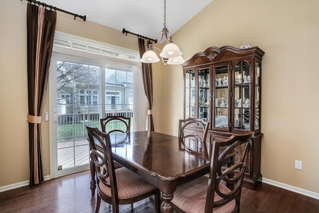 dining room featuring dark wood-style flooring, baseboards, a notable chandelier, and lofted ceiling