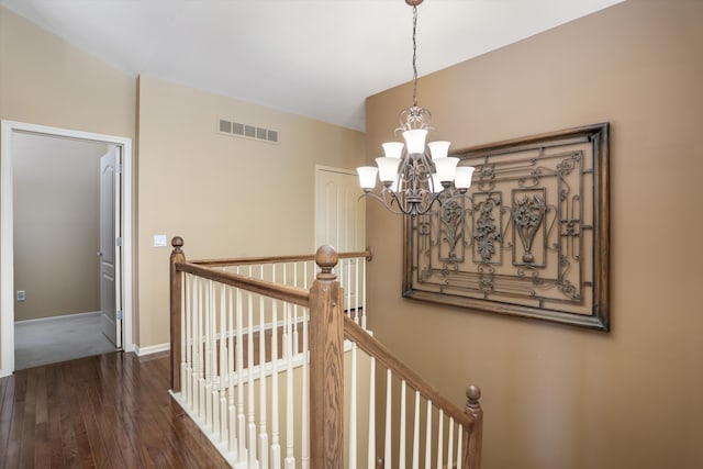 stairway with a notable chandelier, visible vents, baseboards, and hardwood / wood-style flooring