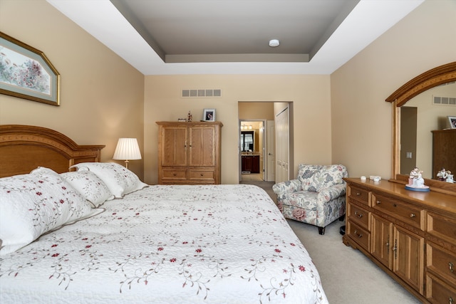 bedroom with a raised ceiling, light carpet, ensuite bath, and visible vents