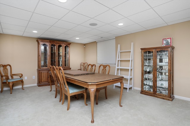 dining room featuring baseboards, a drop ceiling, and light carpet
