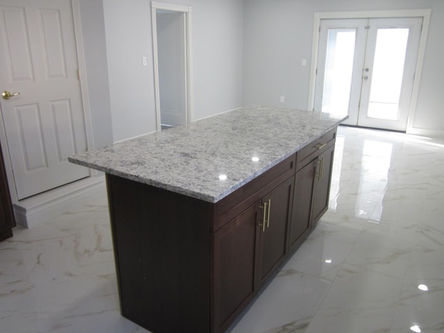 kitchen featuring light stone countertops, dark brown cabinetry, french doors, marble finish floor, and a kitchen island