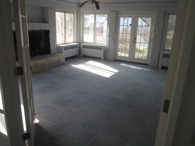 unfurnished living room with radiator heating unit, ceiling fan, a fireplace, and french doors
