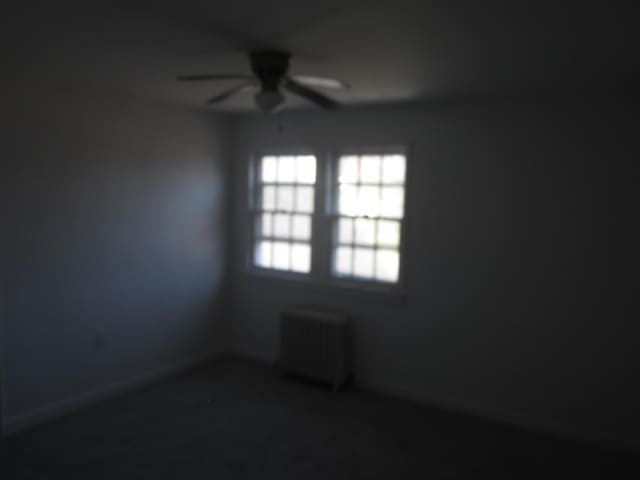 unfurnished room with a ceiling fan, baseboards, and radiator