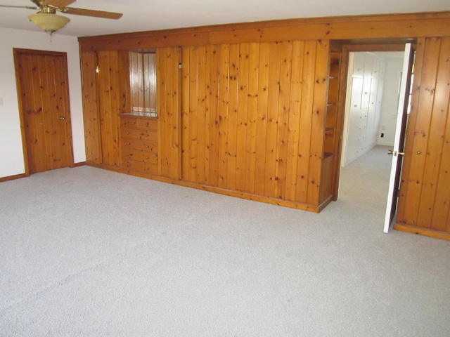 unfurnished room with a ceiling fan, baseboards, wood walls, and carpet