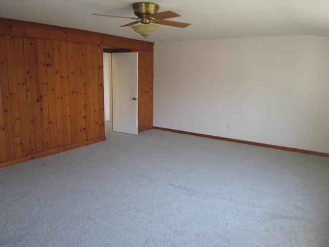 empty room featuring baseboards, light carpet, a ceiling fan, and wood walls