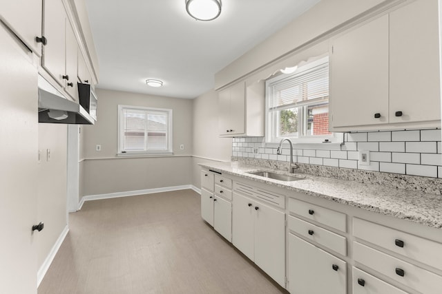 kitchen with light stone countertops, a sink, white cabinetry, baseboards, and backsplash