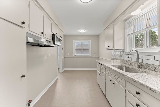 kitchen with baseboards, a sink, white cabinetry, and under cabinet range hood