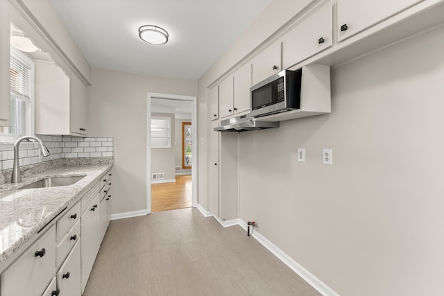 kitchen featuring decorative backsplash, baseboards, stainless steel microwave, white cabinets, and a sink
