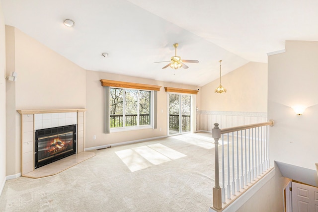 unfurnished living room with ceiling fan, visible vents, a tiled fireplace, lofted ceiling, and carpet flooring