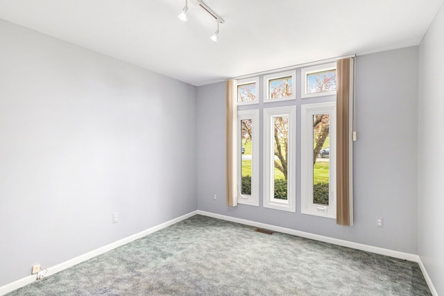 empty room with carpet floors, baseboards, visible vents, and track lighting