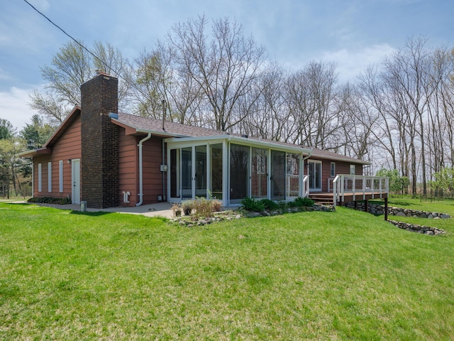 rear view of property featuring a lawn, a wooden deck, a chimney, and a sunroom