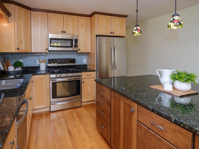 kitchen with appliances with stainless steel finishes, a sink, light wood finished floors, dark stone counters, and backsplash