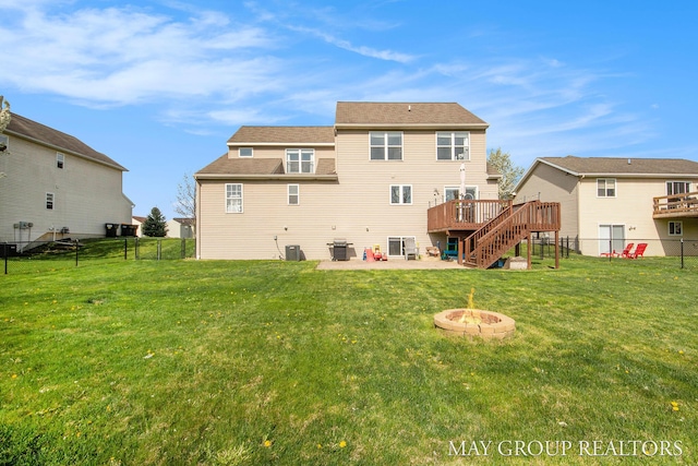 back of property with a deck, stairway, a fenced backyard, a lawn, and a fire pit