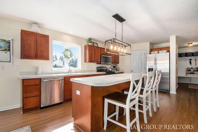 kitchen featuring a breakfast bar, light countertops, a center island, stainless steel appliances, and wood finished floors