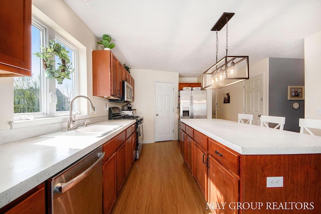 kitchen featuring pendant lighting, light countertops, a sink, light wood finished floors, and appliances with stainless steel finishes