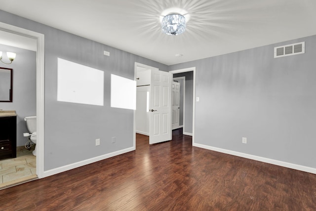 unfurnished bedroom featuring an inviting chandelier, a walk in closet, baseboards, wood finished floors, and visible vents