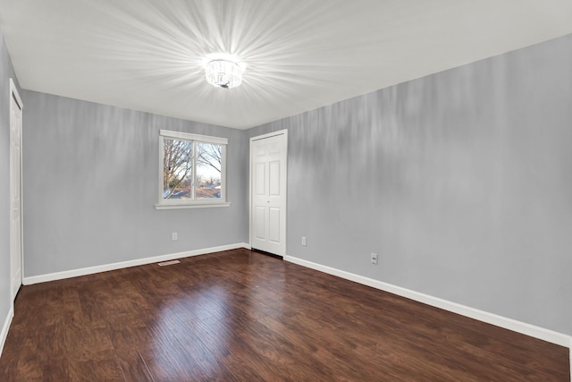 unfurnished room featuring a notable chandelier, baseboards, and dark wood finished floors