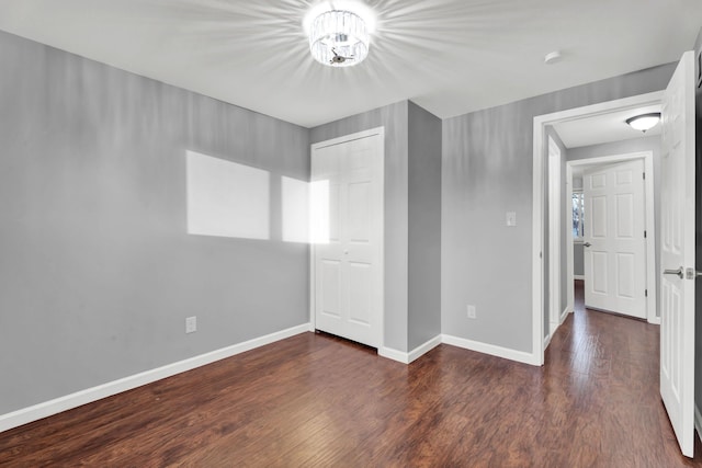 unfurnished bedroom with baseboards, a chandelier, wood finished floors, and a closet