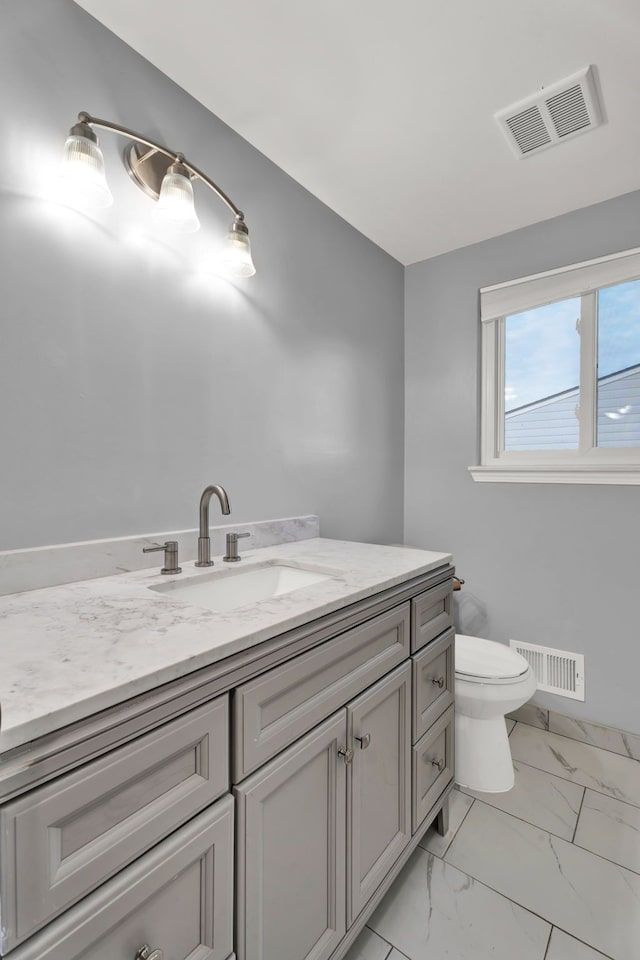 bathroom with vanity, toilet, marble finish floor, and visible vents