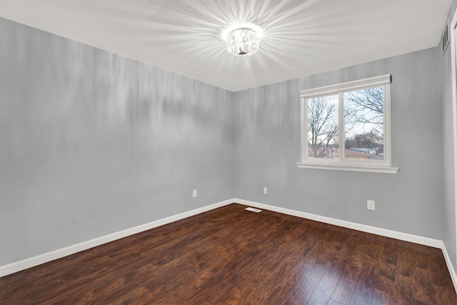 empty room featuring baseboards, a notable chandelier, and wood finished floors