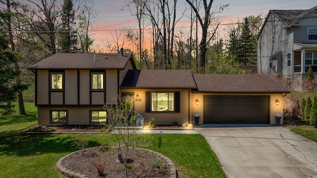 split level home with a garage, a shingled roof, a front yard, and concrete driveway