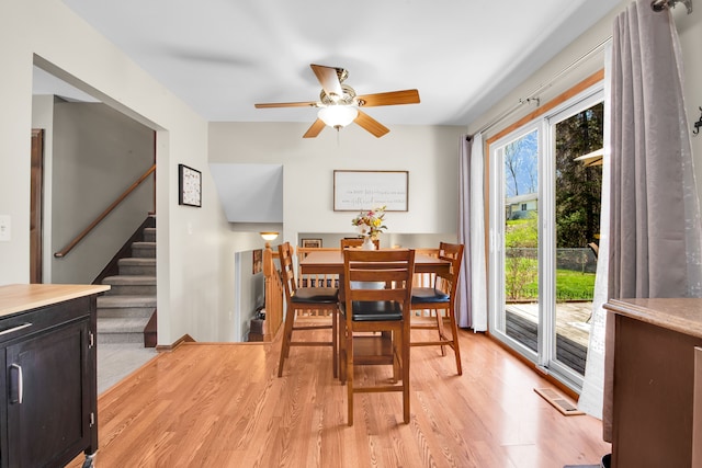 dining area featuring light wood-type flooring, stairs, ceiling fan, and visible vents