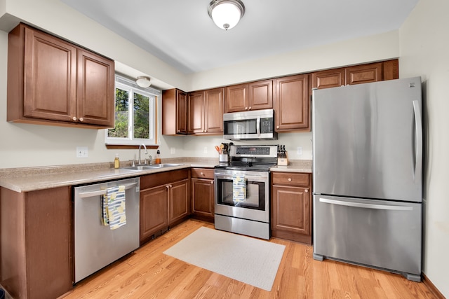 kitchen with a sink, appliances with stainless steel finishes, light wood-type flooring, and light countertops
