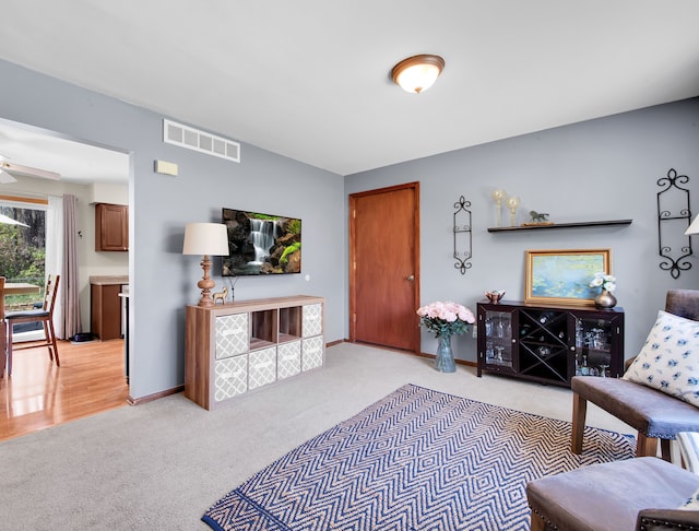 living room with baseboards, visible vents, a ceiling fan, and light colored carpet