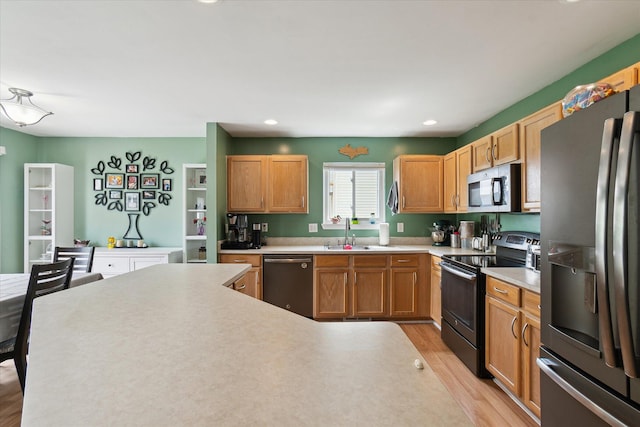 kitchen with appliances with stainless steel finishes, a sink, light countertops, light wood-style flooring, and recessed lighting