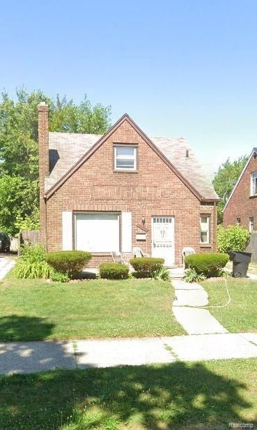 view of front of home with brick siding, roof with shingles, a front yard, and a chimney