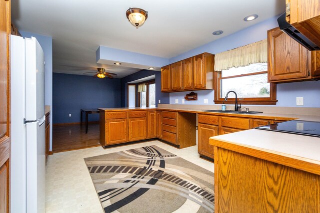 kitchen featuring freestanding refrigerator, a peninsula, ventilation hood, brown cabinets, and a sink