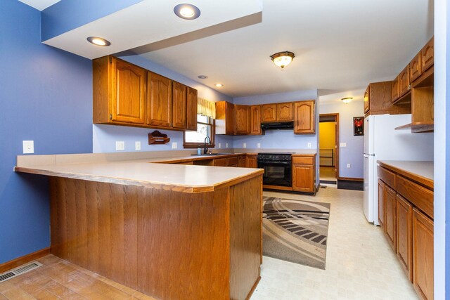 kitchen featuring black / electric stove, brown cabinets, a sink, a peninsula, and under cabinet range hood