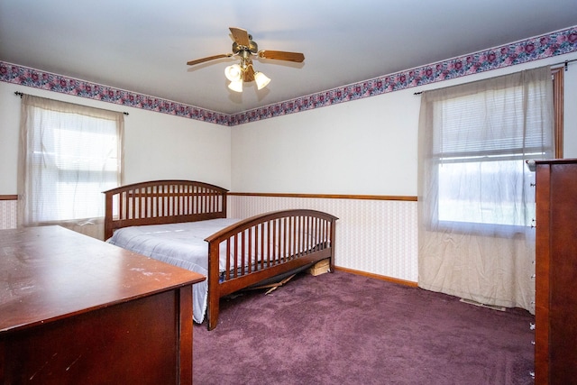 carpeted bedroom featuring a wainscoted wall, multiple windows, and ceiling fan