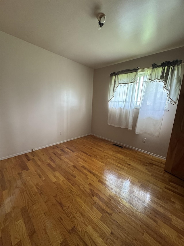 spare room featuring baseboards, wood finished floors, and visible vents