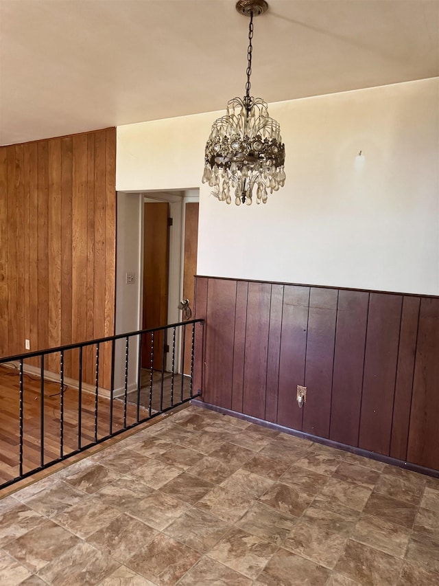empty room featuring stone finish flooring, a chandelier, and wooden walls
