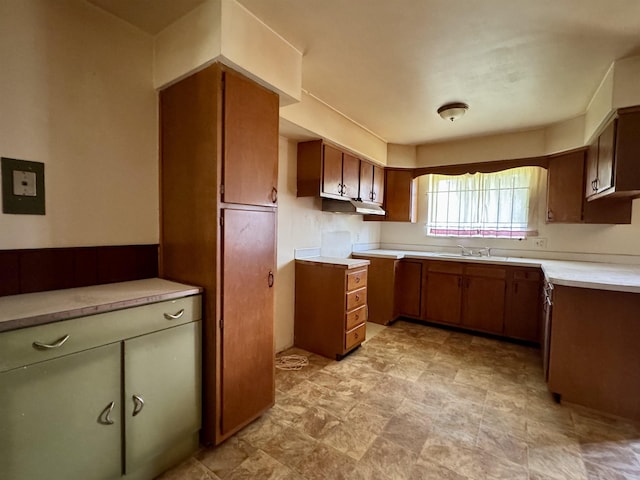 kitchen featuring light countertops, under cabinet range hood, brown cabinets, and a sink