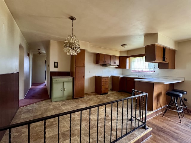 kitchen with a peninsula, light countertops, brown cabinets, a notable chandelier, and hanging light fixtures