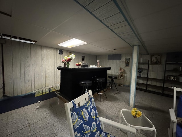 finished basement featuring a dry bar, a paneled ceiling, and wood walls