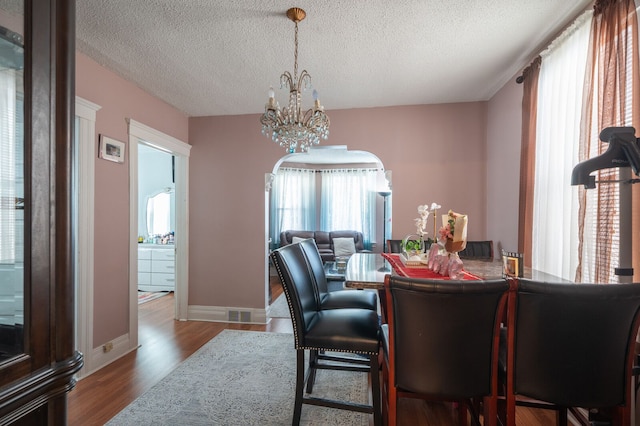 dining room with wood finished floors, visible vents, a textured ceiling, and a chandelier
