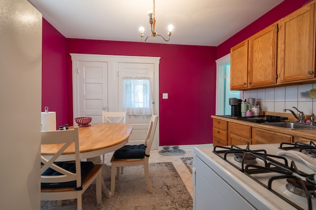 kitchen with brown cabinets, a notable chandelier, a sink, white gas range, and backsplash