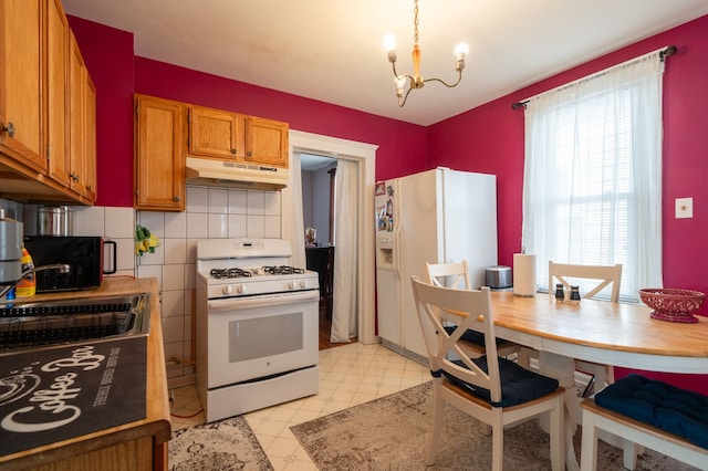 kitchen with white appliances, light floors, under cabinet range hood, brown cabinets, and a notable chandelier