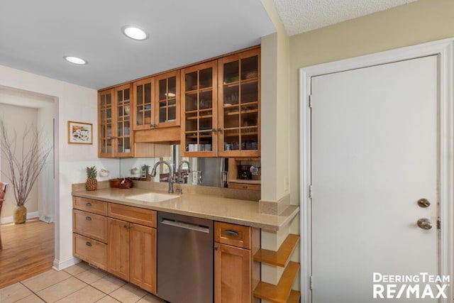 kitchen featuring a sink, light countertops, baseboards, stainless steel dishwasher, and glass insert cabinets