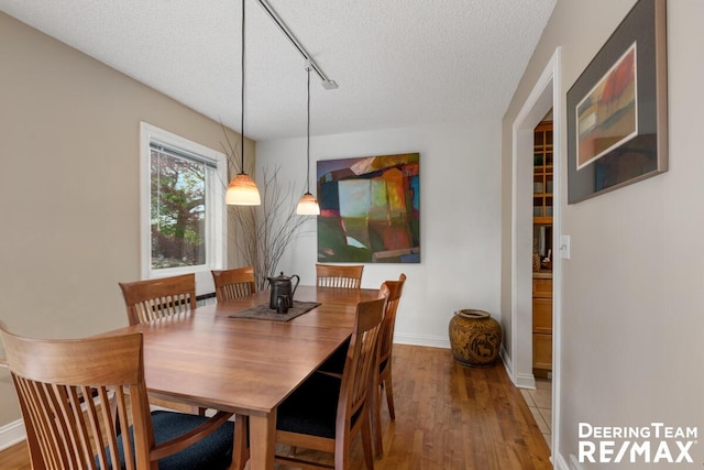 dining area with baseboards, rail lighting, a textured ceiling, and wood finished floors